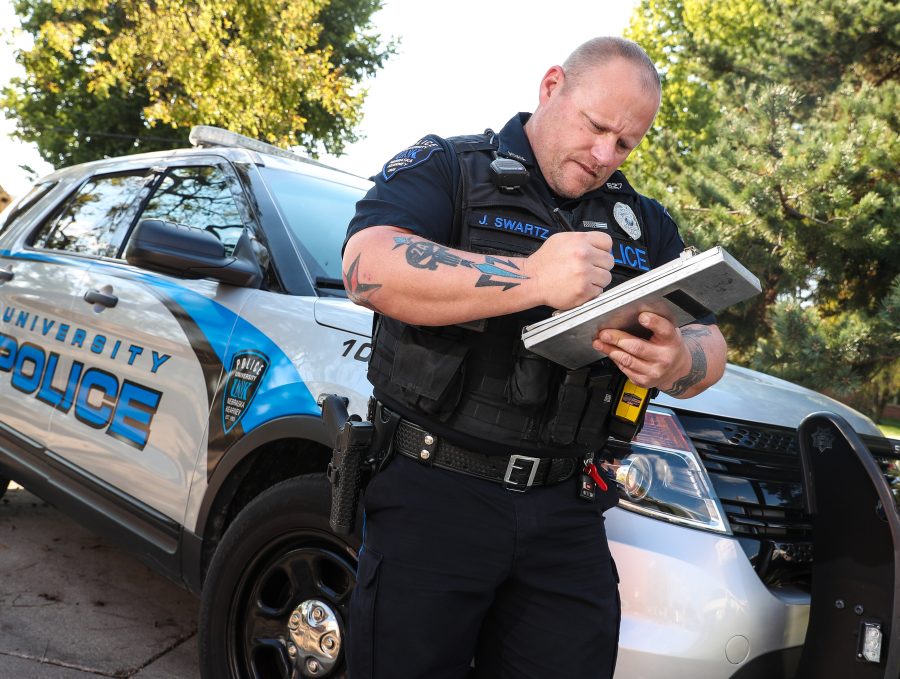 UNK officer stands in front of police cruiser while writing ticket.